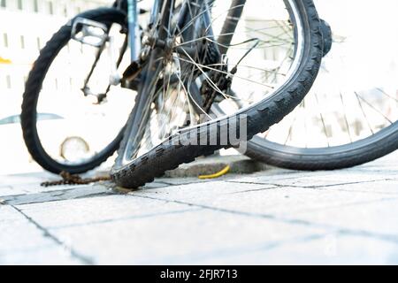 Der verbogene Hinterreifen eines Fahrrads in der Stadt mit zerstörter Kette. Stockfoto
