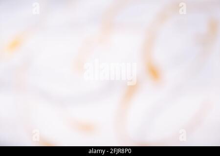 Verschwommener weißer und goldener Hintergrund mit Wellenmuster. Defokussierte, abstrakte Hintergrundkulisse mit verwacklungsunschärfen und Bokeh. Unscharfe beigefarbene Tapete. Stockfoto