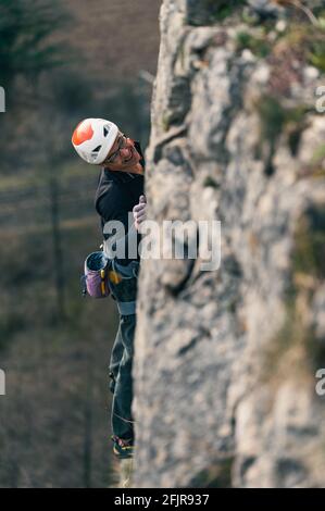 Der Mensch klettert auf eine senkrechte Wand mit Helm und verwischtem Felsen im Vordergrund. Stockfoto