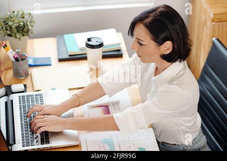 Junge Geschäftsfrau, die mit Finanzdokumenten arbeitet und das Formular ausfüllt Laptop erstellt Bericht Stockfoto