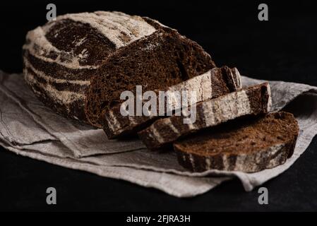 Handwerklich geschnittenes Roggenbrot. Nahaufnahme von Scheiben frisch gebackenem Sauerteig-Brot auf dunklem Hintergrund. Low-Taste. Selektiver Fokus Stockfoto