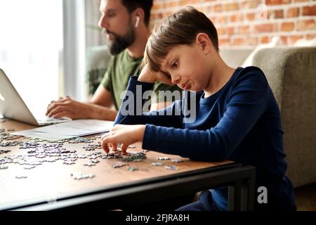 Langeweile Junge lösen Puzzle während Vater arbeiten Stockfoto