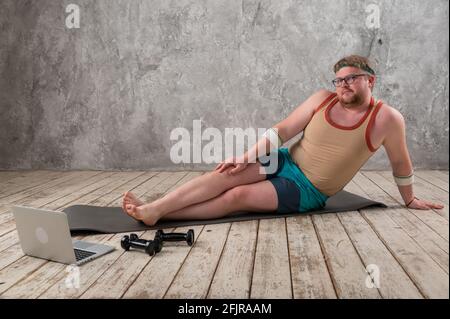 Lustige fette Mann tun Sport auf der Yoga-Matte, Sport treiben online, Blick in den Laptop Stockfoto