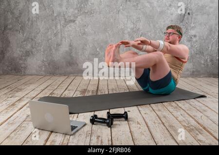 Lustige fette Mann in Sportkleidung tun Übungen. Er spielt aus der Ferne Sport, während er auf seinen Laptop schaut Stockfoto