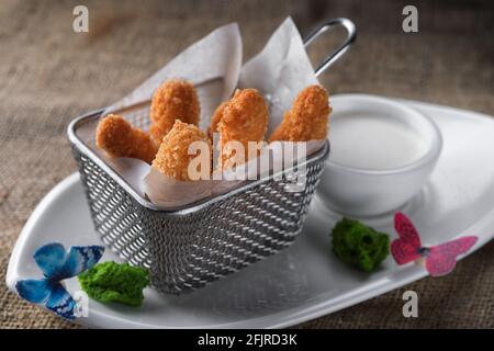 Nuggets mit Sauce auf einem weißen Teller, in einem Metallkorb Stockfoto