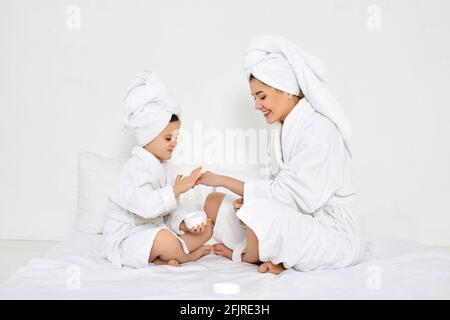Mutter und Tochter tragen in weißen Bademänteln Creme auf Stockfoto