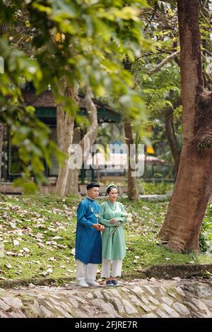 Glückliches junges vietnamesisches Paar in AO dai Kleider Blick auf Teichwasser im Stadtpark verbringen Tag nach der Zeremonie zusammen Stockfoto