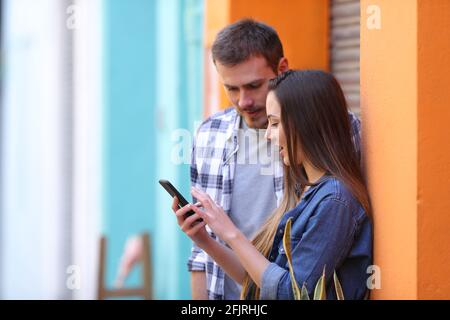 Zwei Freunde, die ihr Smartphone nutzen, sprechen über das Stehen von Online-Inhalten In einer bunten Straße Stockfoto
