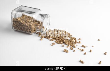 Glasflasche mit verschütteten goldenen Nuggets auf weißem Hintergrund Stockfoto