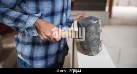 Hübsche junge Arbeiterin mit blauem Arbeitsshirt, die auf der Baustelle arbeitet und einen schwarzen Gummihammer in der Hand hält, innen, Konzept einer weiblichen Frau Stockfoto