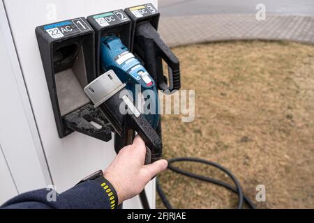 Elektrische Tankstelle für Elektrofahrzeuge. Der Mann nimmt den Kontaktdraht, um die Maschine anzuschließen Stockfoto