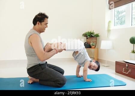 Ein fröhlicher Vater hilft seinem lachenden Kind beim Praktizieren des Handstandes zu Hause Stockfoto