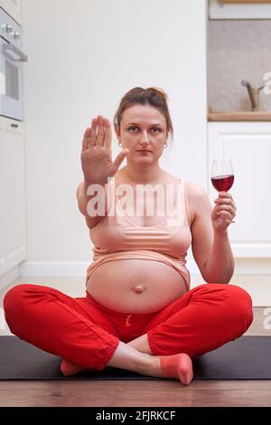 Fitness während der Schwangerschaft und Abstinenz vom Weintrinken. Eine Schwangerin bei einem Sporttraining zu Hause zeigt eine Stop-Geste als Zeichen eines gi Stockfoto