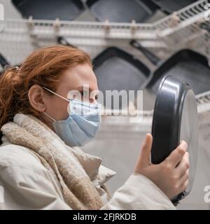 Frau in einer medizinischen Gesichtsmaske wählt eine Bratpfanne Im Geschäft Stockfoto