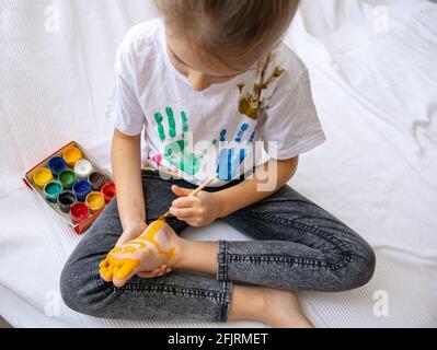 Das Kind zeichnet mit einem Pinsel ein Muster auf seinen Fuß. Eine lustige Zeichnung mit hellen Farben auf dem Körper. Stockfoto
