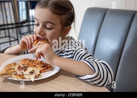 Ein süßes kleines Mädchen isst appetitlich ein Stück Pizza zum Mittagessen. Stockfoto