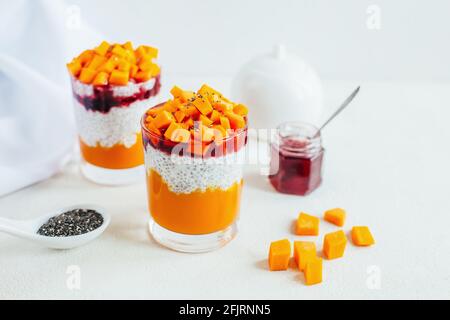 Nahaufnahme von zwei Gläsern mit Chia Pudding Kürbismus und Erdbeermarmelade auf weißem Teller Stockfoto