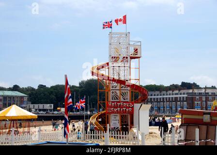 Helter Skelter-Vergnügungsfahrt am Strand, Weymouth, Dorset, England mit Union- und kanadischen Flaggen an der Spitze Stockfoto