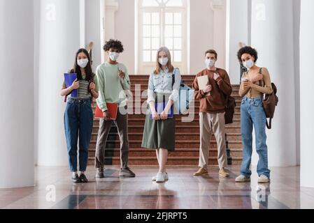 Interracial Studenten in medizinischen Masken halten Notizbücher in der Universität Stockfoto