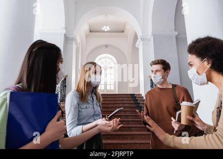 Multiethnische Studenten in Schutzmasken reden in der Halle der Universität Stockfoto