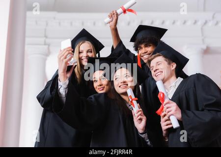 Interracial Absolventen mit Diplomen, die Selfie in der Universität Stockfoto