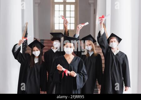 Gemischtrassige Junggesellen in Schutzmasken mit Diplomen Stockfoto