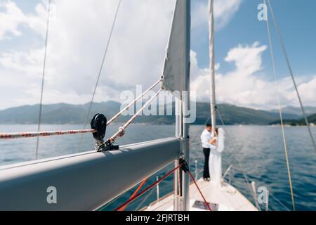 Blick vom Bug einer Segelyacht. Das Brautpaar steht am Heck eines Segelbootes vor der Kulisse der Berge Stockfoto