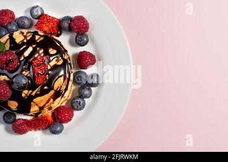 Draufsicht auf ein Dessert aus Pfannkuchen mit Früchten und Schokolade auf weißem Teller auf rosa Hintergrund Stockfoto