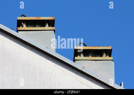 Zwei große Kamine auf dem verlassenen Industriegebäude mit Mesh-Schutz oben mit verrosteten Metallkappen bedeckt Hintergrund des klaren blauen Himmels Stockfoto