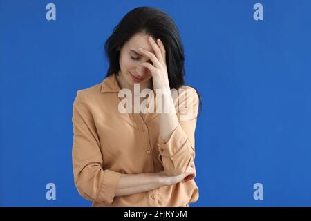 Traurige Frau, die ihren Kopf auf blauem Hintergrund hält Stockfoto