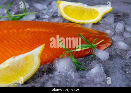 Frisches, rohes Lachsfischsteak mit Gewürzen auf Eis auf dunklem Steingrund. Kreatives Layout aus Fisch, Draufsicht, Flachlage Stockfoto