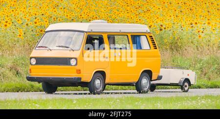 Retro orange Camper Bus mit Popup Camper fahren neben einem Feld mit Sonnenblumen Stockfoto