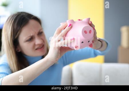 Junge Frau schüttelt Sparschwein mit Geld Stockfoto