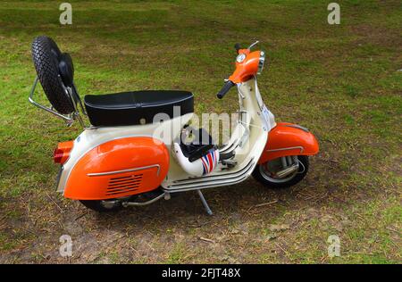 Orange und weiße Lambretta Motorroller auf Gras geparkt Stockfoto