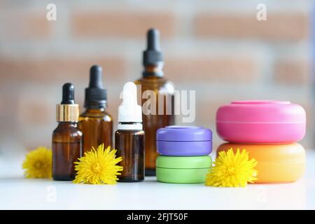 Viele Flaschen und Gläser mit Kosmetika liegen auf dem Tisch mit Gelbe Blüten aus der Nähe Stockfoto