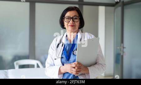 Porträt einer älteren Ärztin, die im Krankenhaus steht und die Kamera anschaut. Stockfoto