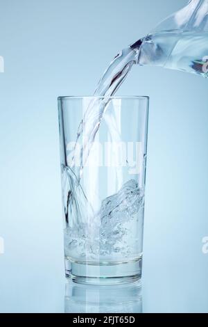 Das klare Glas wird mit Wasser aus dem Auslauf des Glaskänkels gefüllt ein Wasserstrahl mit Spritzern und Blasen sättigt und befeuchtet, niemand. Stockfoto