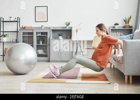 Junge Schwangerin, die im Wohnzimmer Sportübungen macht Zu Hause Stockfoto
