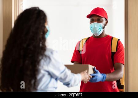 Schwarzer Lieferer in medizinischer Maske, der der Frau eine Schachtel gab Stockfoto