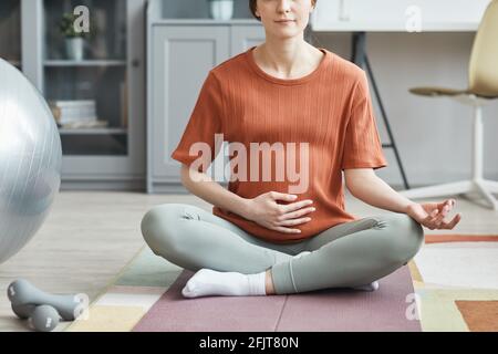 Nahaufnahme einer Schwangeren, die auf einer Trainingsmatte sitzt und meditiert Im Zimmer zu Hause Stockfoto
