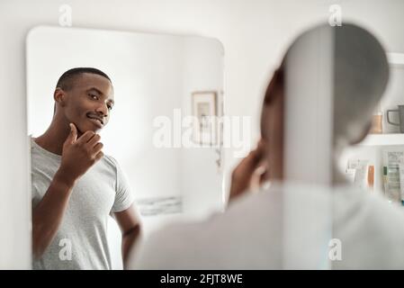 Lächelnder afrikanischer Mann, der in einem Badezimmer auf sein Gesicht schaut Spiegel Stockfoto