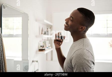 Lächelnder junger afrikanischer Mann, der in seinem Badezimmer auf köln sprüht Stockfoto