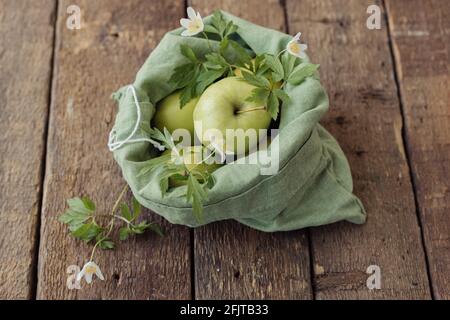 Zero Waste Shopping-Konzept. Frische Äpfel in Öko-Baumwollbeutel auf rustikalem Holztisch. Kunststoff verbieten. Bio-Äpfel und -Blumen in grüner Mehrwegtasche. Eco Stockfoto