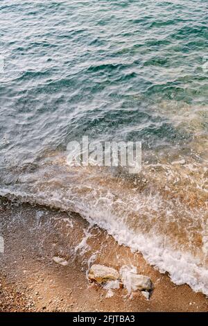 Die Welle rollt über den Strand, auf dem die Steine liegen Lüge Stockfoto