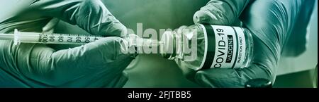 Nahaufnahme eines Gesundheits- oder Laborarbeiters, das OP-Handschuhe trägt und eine Spritze aus einem simulierten Fläschchen eines Covid-19-Impfstoffs in einem Panorama-f füllt Stockfoto