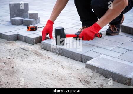 Der Meister in gelben Handschuhen legt Pflastersteine Stockfoto