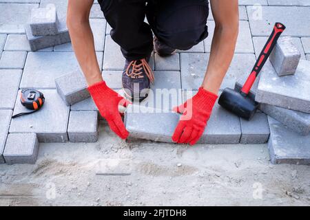 Der Meister in gelben Handschuhen legt Pflastersteine Stockfoto