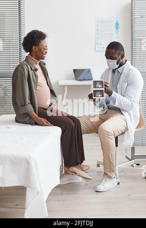 Afrikanischer Arzt untersucht das Ultraschallbild und spricht mit Schwangeren Frau im Krankenhaus verschreibt er Behandlung für sie Stockfoto