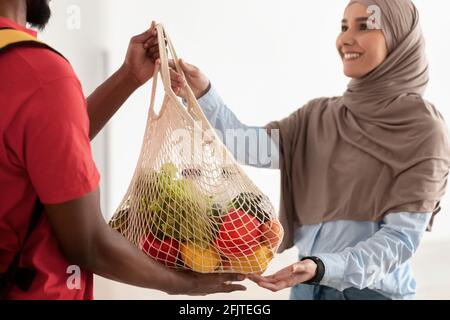 Schwarzer Lieferer, der Netzmaschentasche mit Lebensmitteln gibt Stockfoto