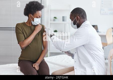 Afrikanischer Arzt im weißen Mantel, der während ihrer Schwangerschaft impft Besuch im Krankenhaus Stockfoto